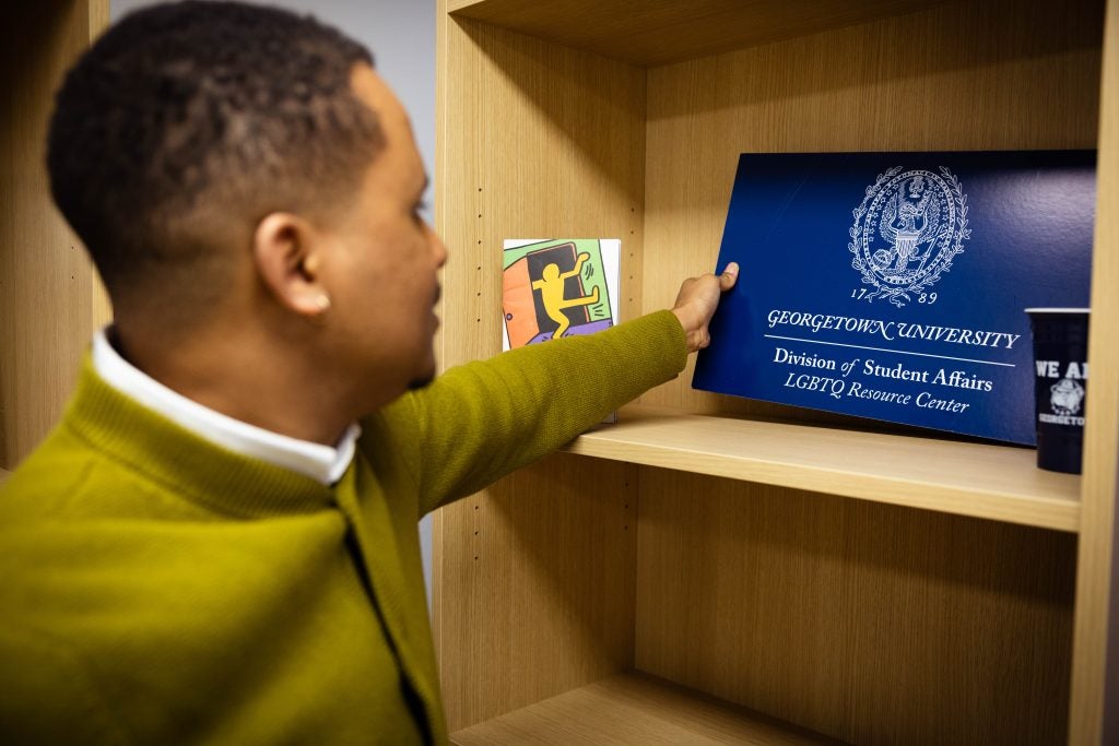 A man in a green sweater reaches out to hold a plaque that says "Georgetown University: Division of Student Affairs LGBTQ Resource Center"