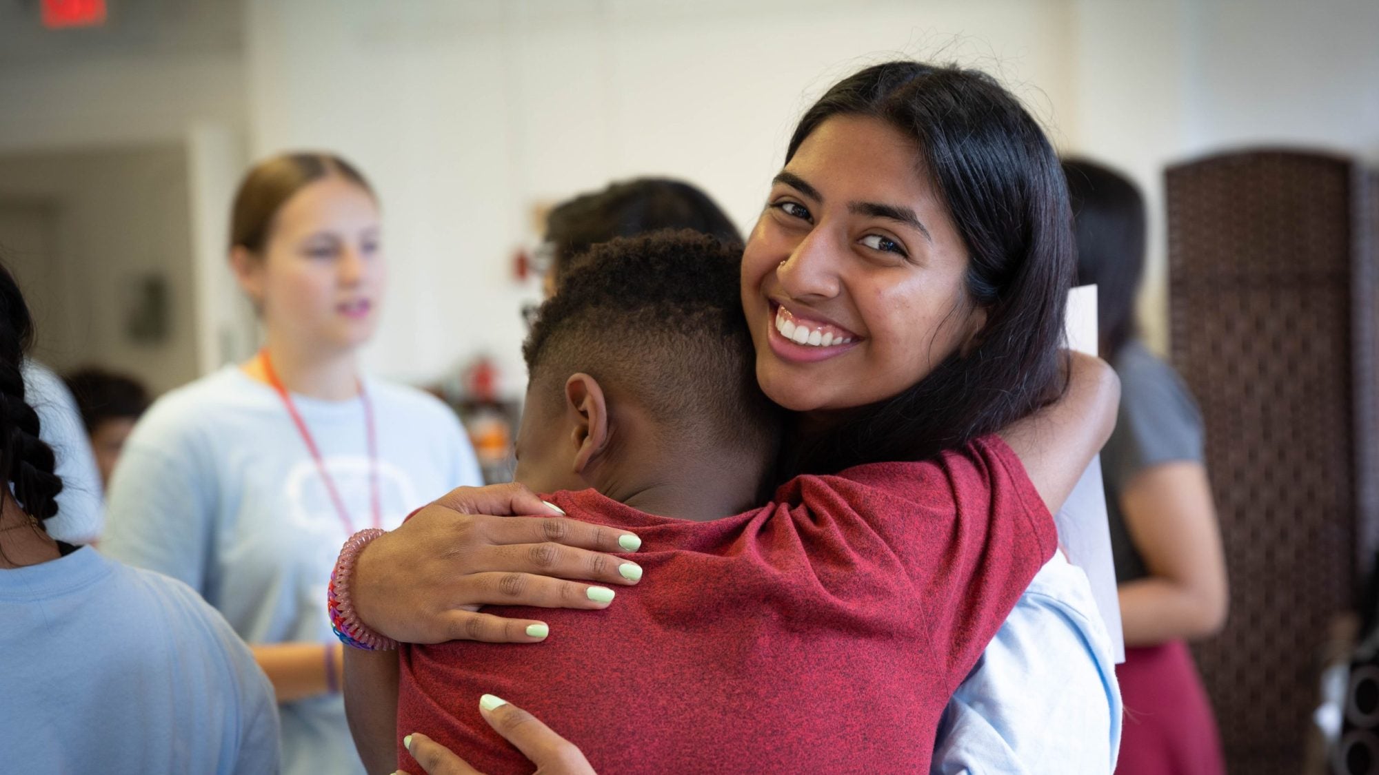 A college student hugs a grade-school student whom she volunteers with and smiles big.