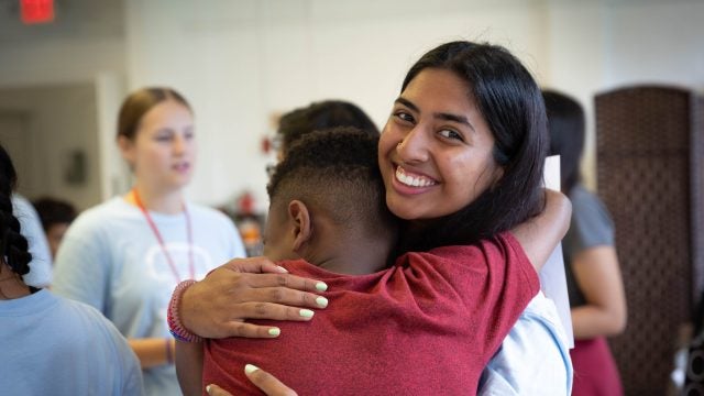 A college student hugs a grade-school student whom she volunteers with and smiles big.