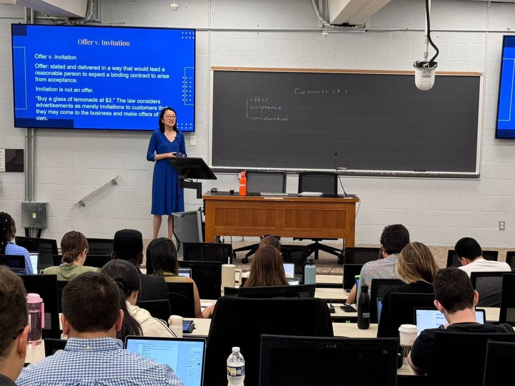 A professor stands by a blackboard in a classroom while teaching a class.