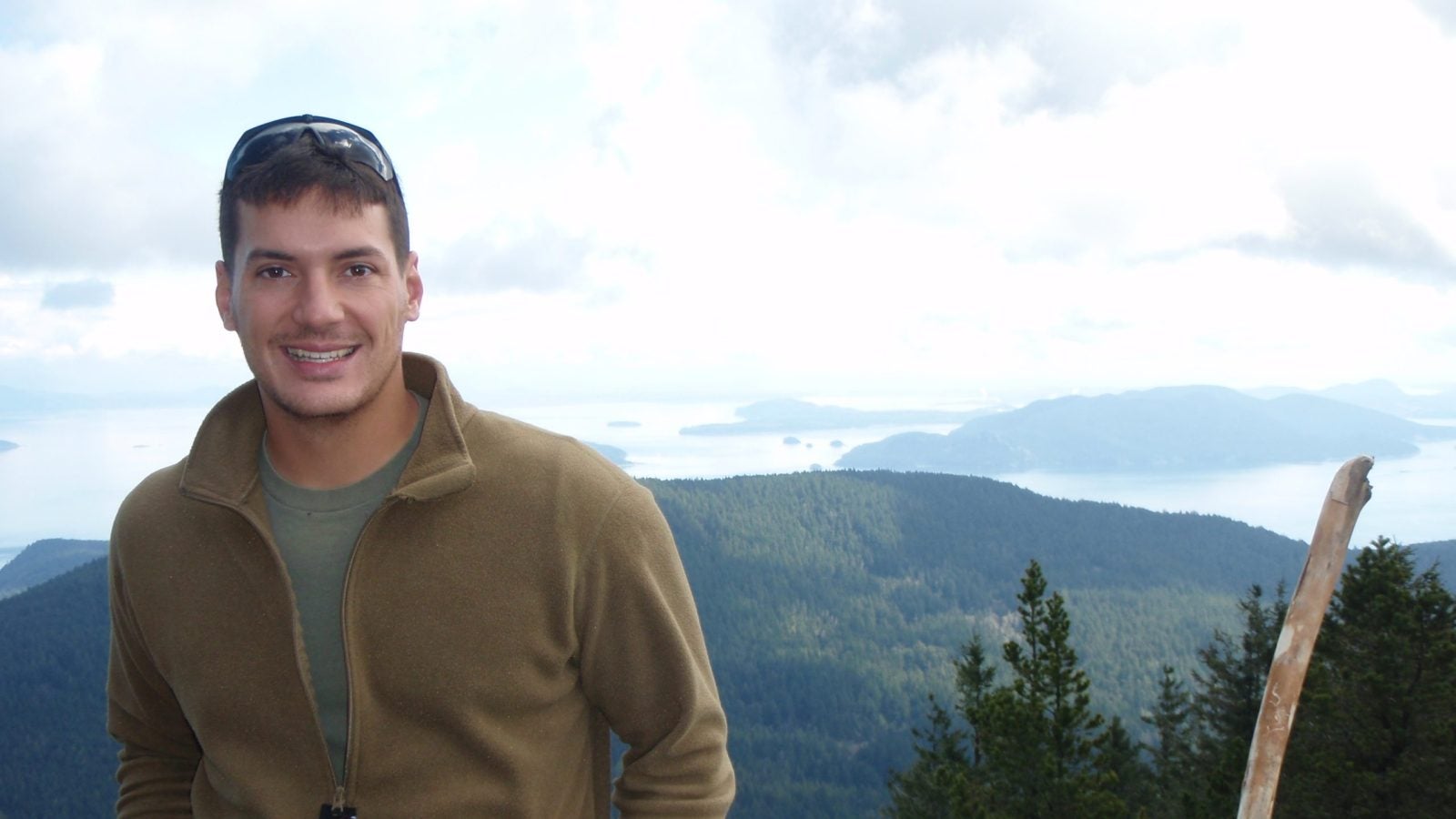 Austin Tice in a tan half-zip sweatshirt with a mountain range in the background