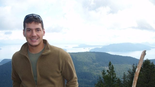 Austin Tice in a tan half-zip sweatshirt with a mountain range in the background