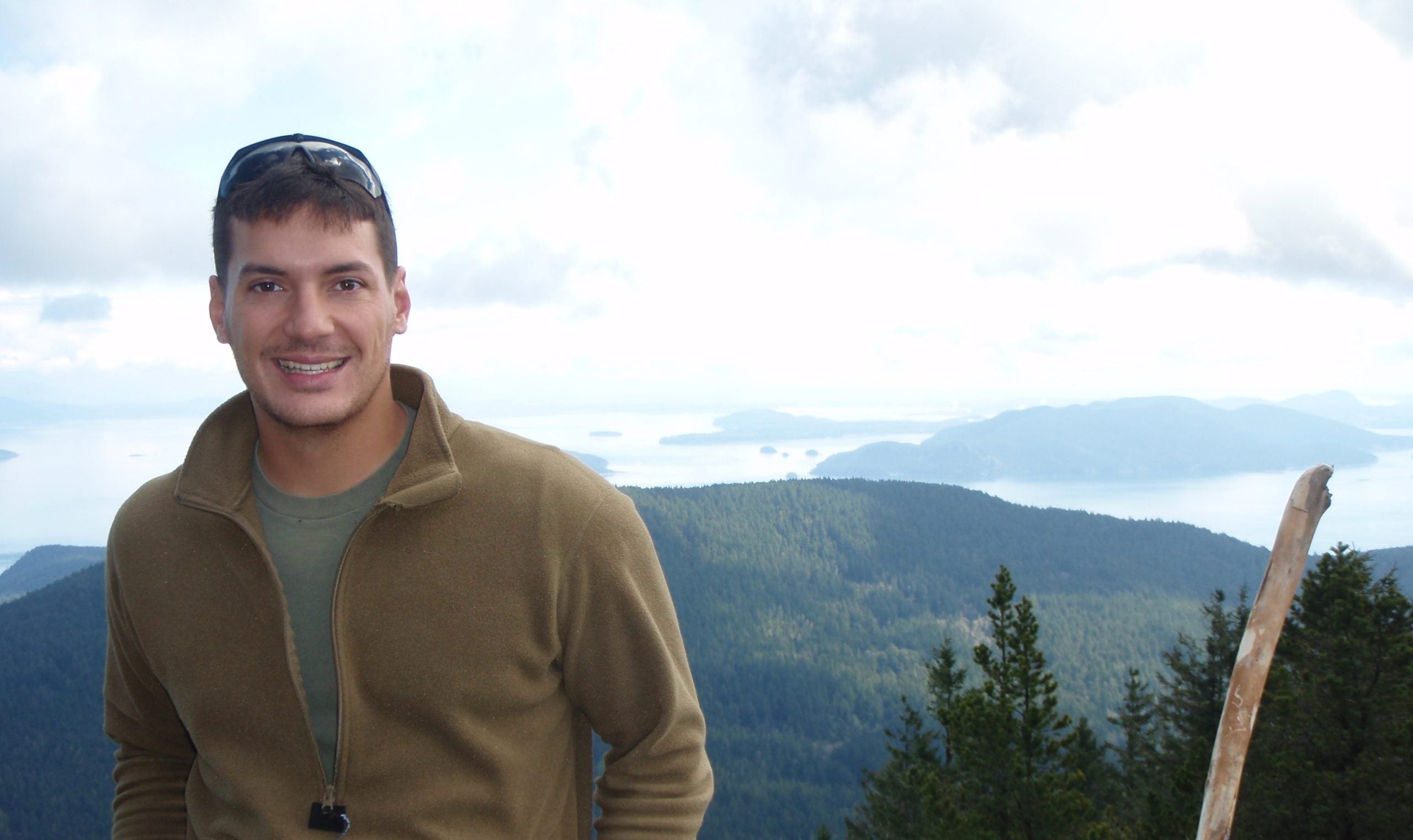 Austin Tice in a tan half-zip sweatshirt with a mountain range in the background