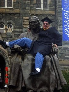 Austin Tice sitting on the John Carroll statue on Healy Lawn in his graduation robe