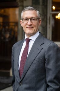 David Edelstein in a gray suit and dark red tie against Healy Hall background