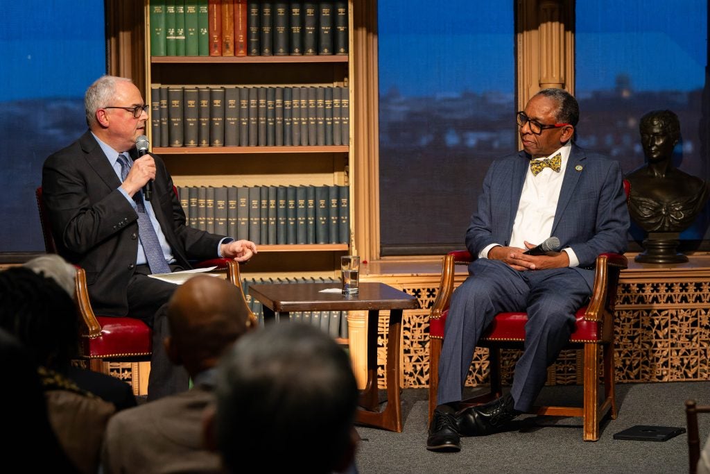 Two men speak to each other in a panel discussion in a library.