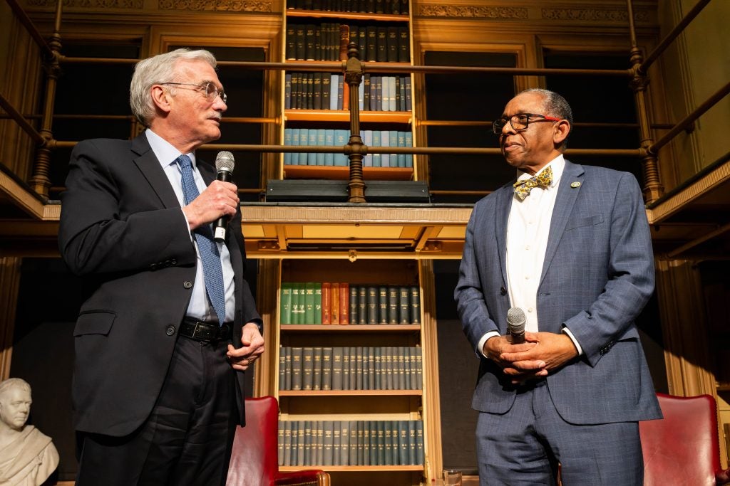 Two men stand on a stage in a library.