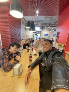 Aire in a black leather coat with a selfie of people at a table in a restaurant