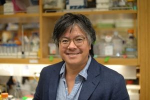 Professor Jeffrey Huang smiles in front of a laboratory.