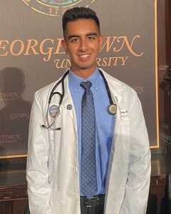 A student wearing a white coat and a stethoscope smiles.