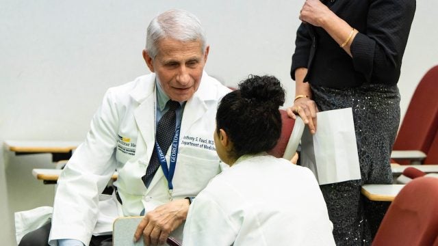 Dr. Fauci, dressed in a white lab coat, meets with a student.