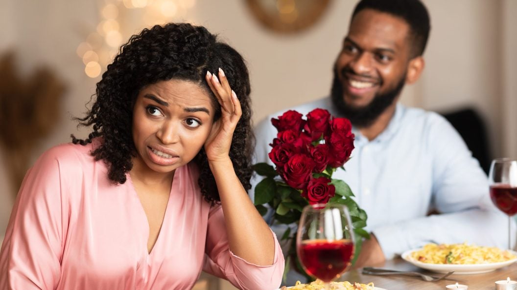 Bad First Impression And Blind Date Concept. Dissatisfied shocked black woman rejecting excited emotional obsessed man who giving her flowers, young couple sitting at table in cafe