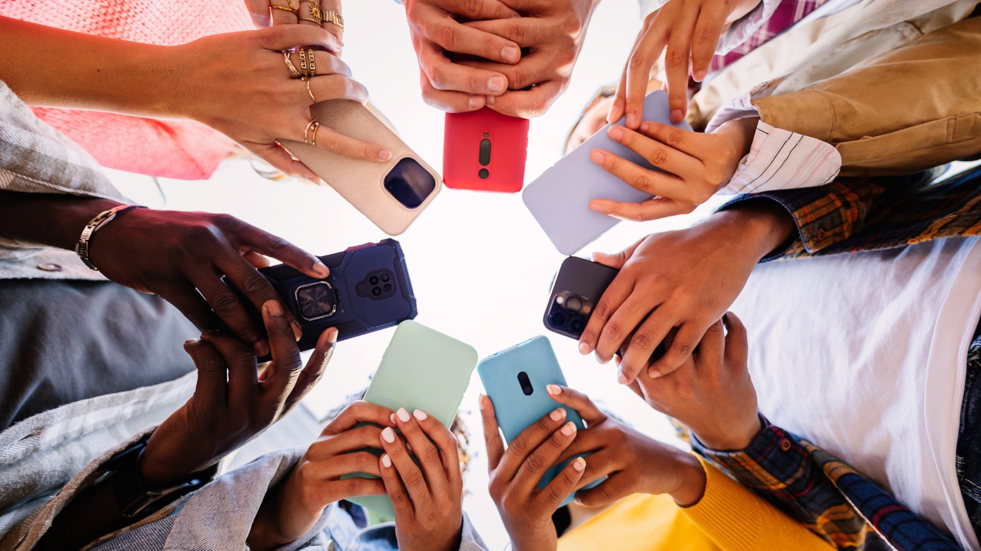 From the ground v iew of 7 people holding phones in their hands in a circle