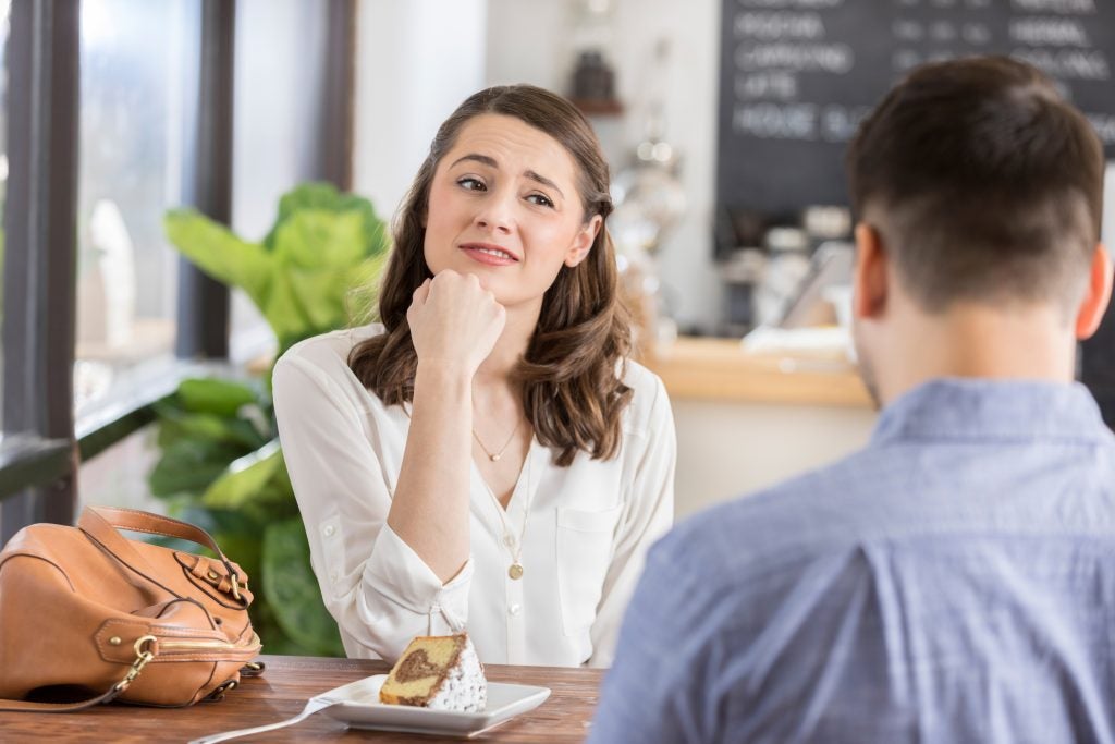 Young woman makes an uneasy or disinterested face while on a blind date in a coffee shop. The back of the young man's head is seen in the foreground.