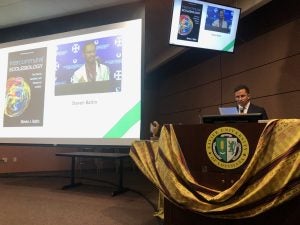 A man gives a presentation from behind a podium with a screen behind him.