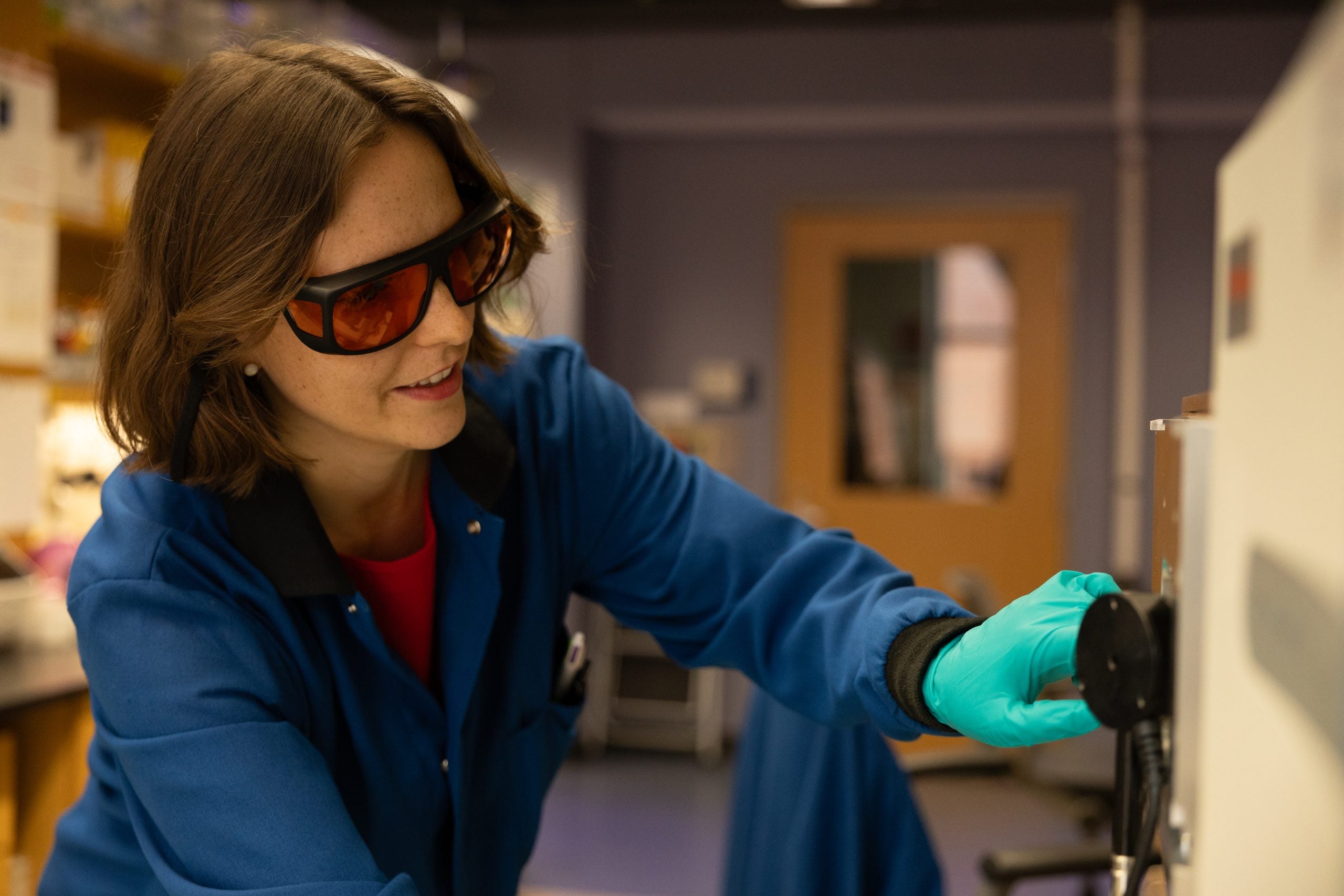 Roussel in a blue lab coat and goggles interacting with lab equipment