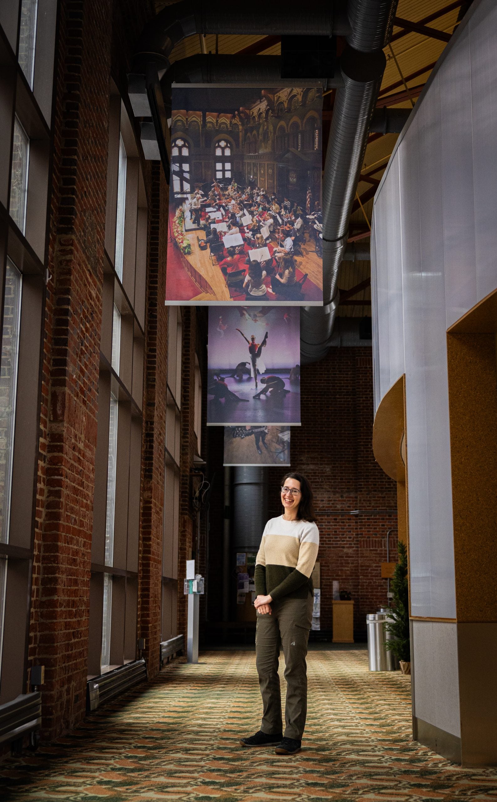 A woman stands under flags in a hallway.