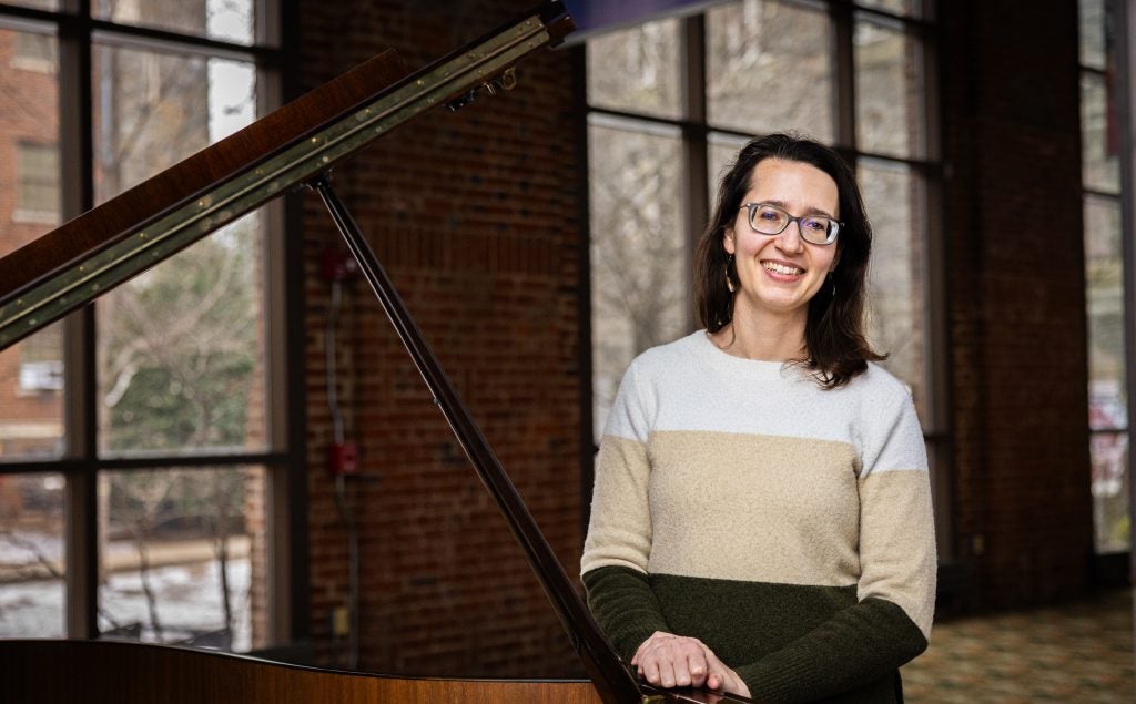 A woman stands next to a grand piano and smiles.