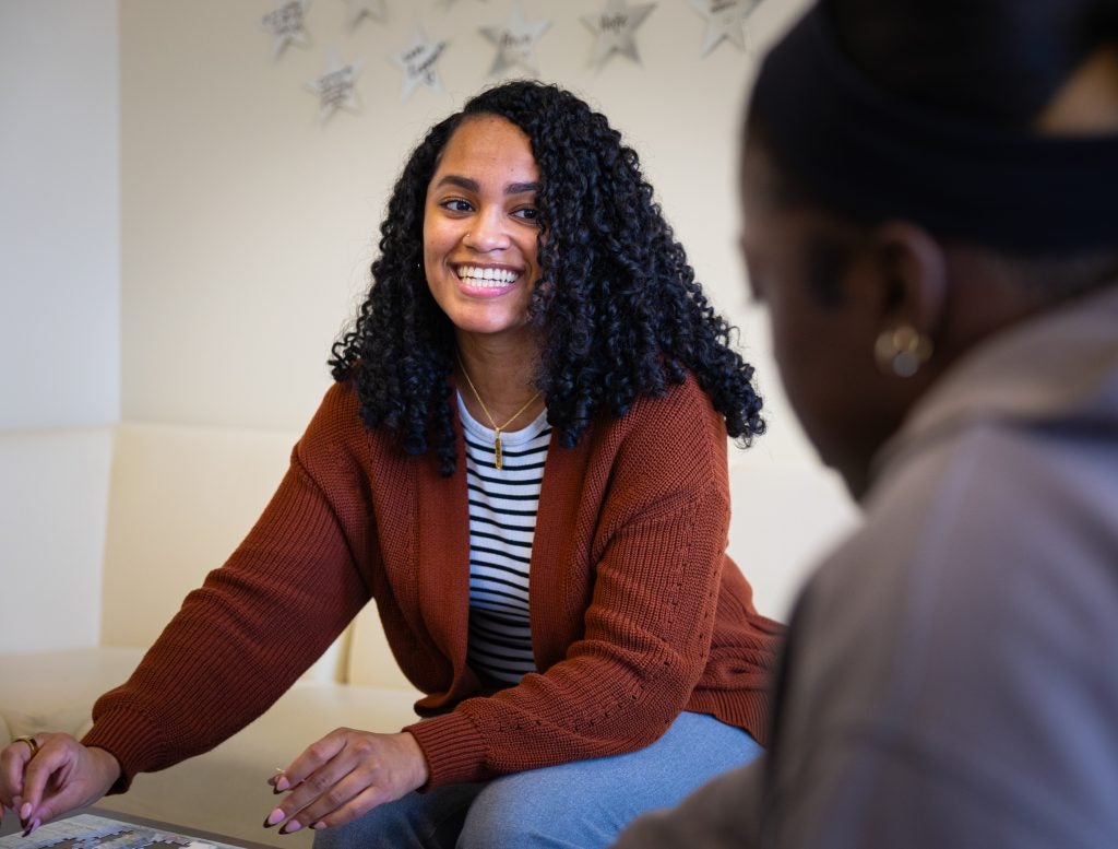 Alexis Green with an orange sweater and striped shirt talks to a young woman