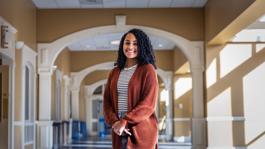 Alexis Green with an orange sweater and striped shirt in a well lit hallway