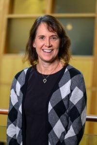 Robin Dillon Merrill indoors with a sweater and black blouse with a necklace