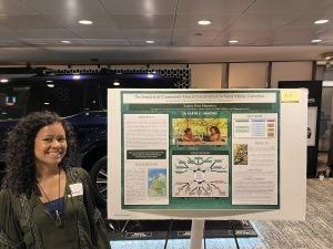 A student smiles next to a poster of her research