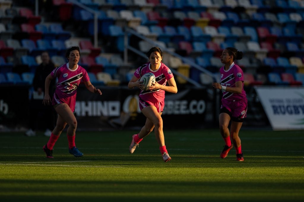 Three young women in pink jerseys play rugby