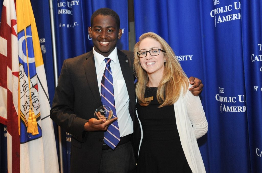 A student and higher education administrator pose together. The student holds an award.