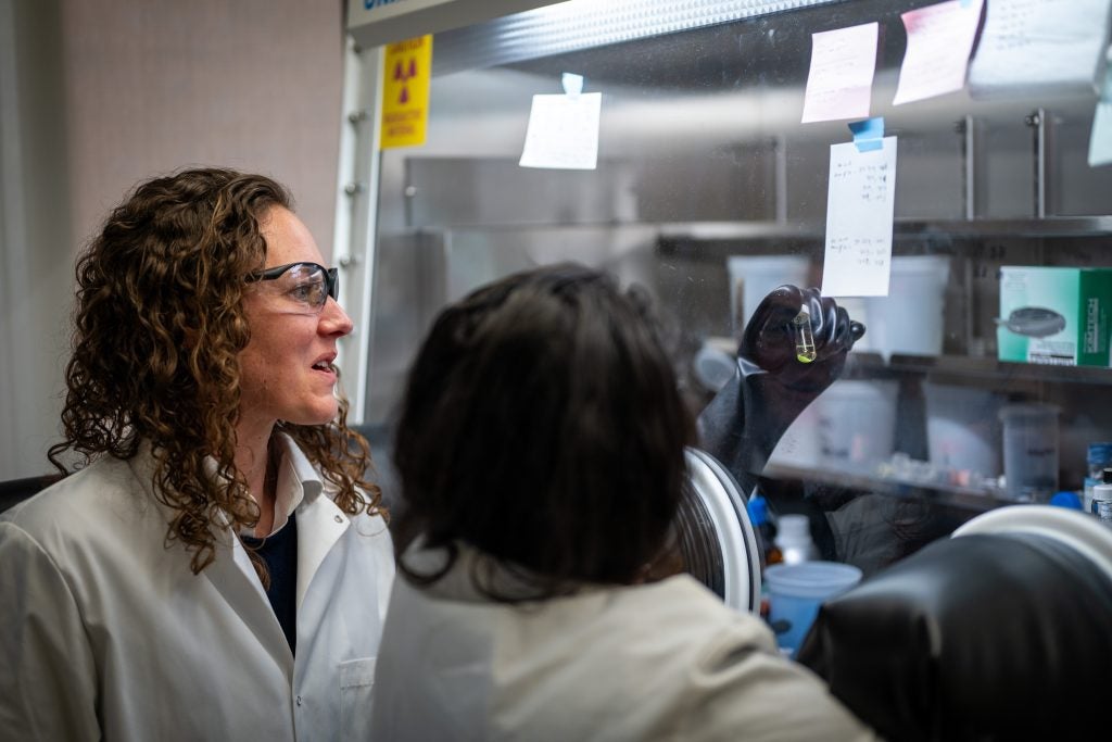 Knope examines a vial in a lab with a student