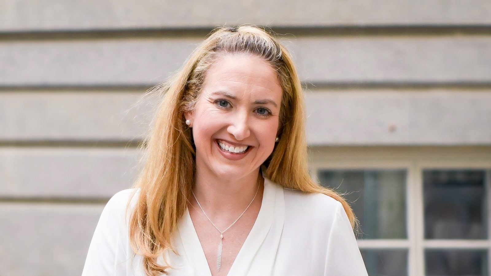 A blonde-haired woman smiles in a white shirt