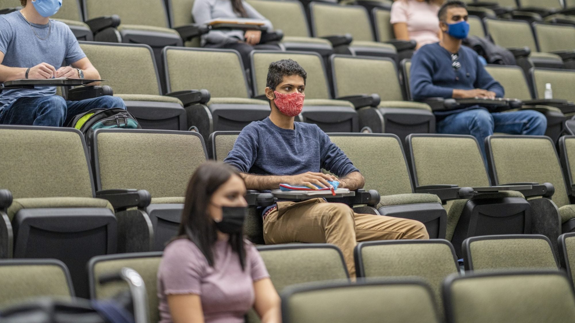 Students sit a few seats apart from each other wearing masks in a lecture hall