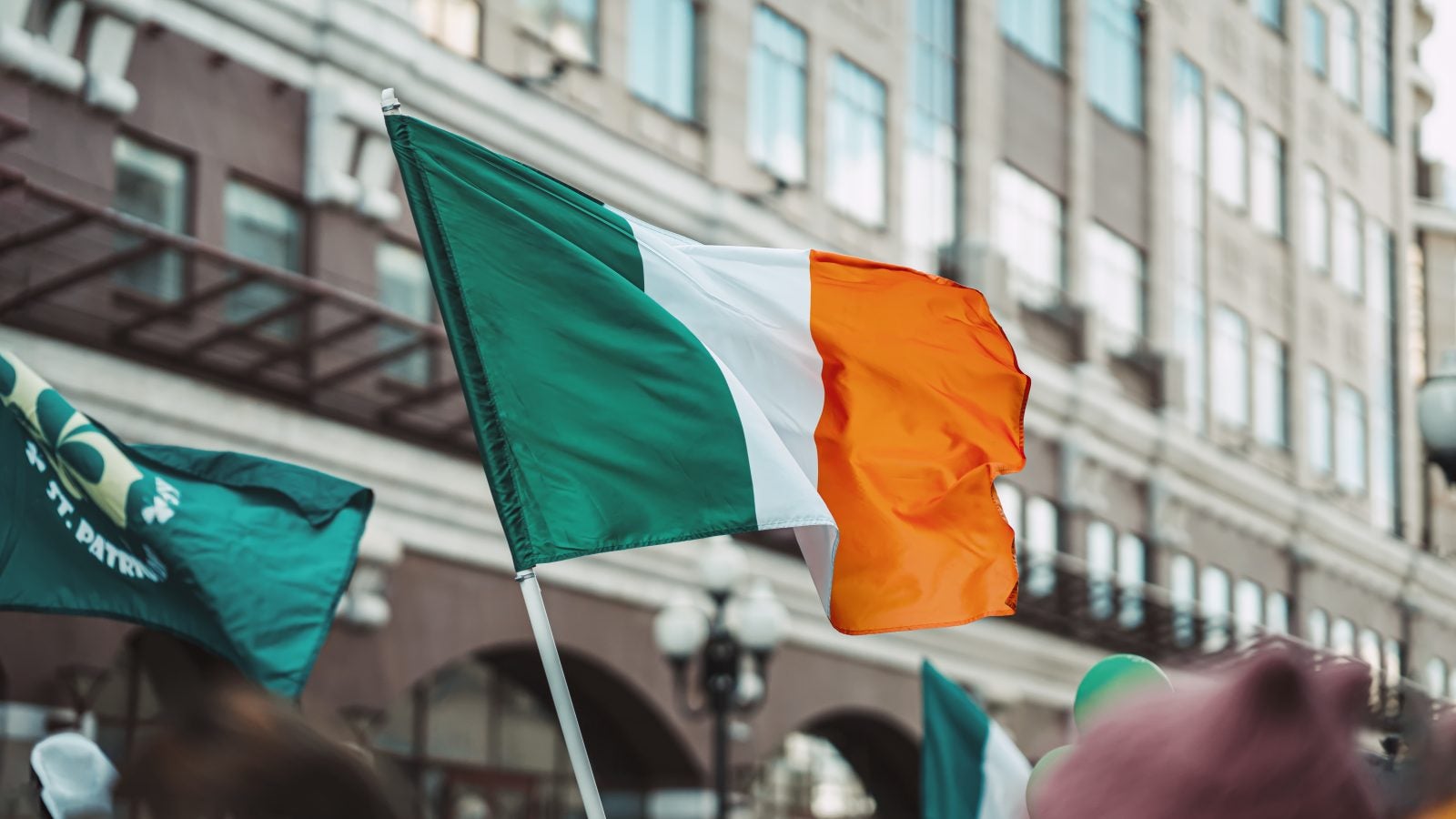 National Flag of Ireland close-up above people crowd, city street, traditional carnival of St. Patrick&#039;s Day