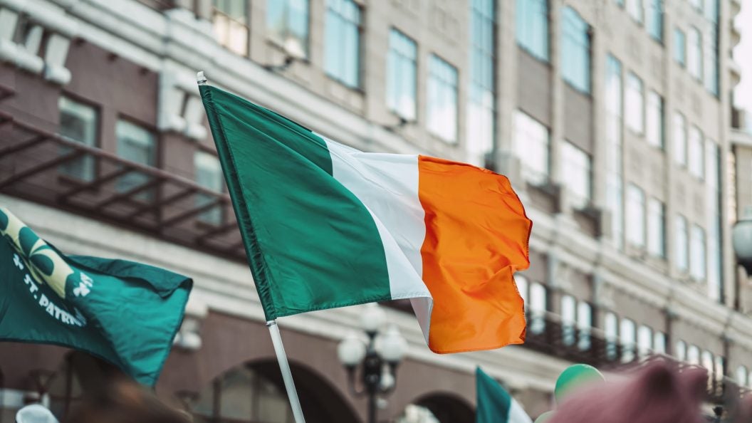 National Flag of Ireland close-up above people crowd, city street, traditional carnival of St. Patrick&#039;s Day