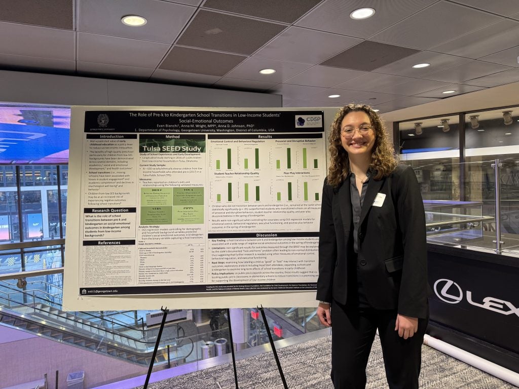 A student stands next to a poster of her research