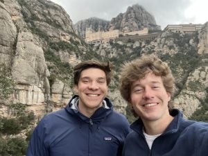 Two young men in front of a mountainside with some buildings on top