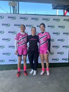 Two women in pink jerseys stand with a coach in a black outfit