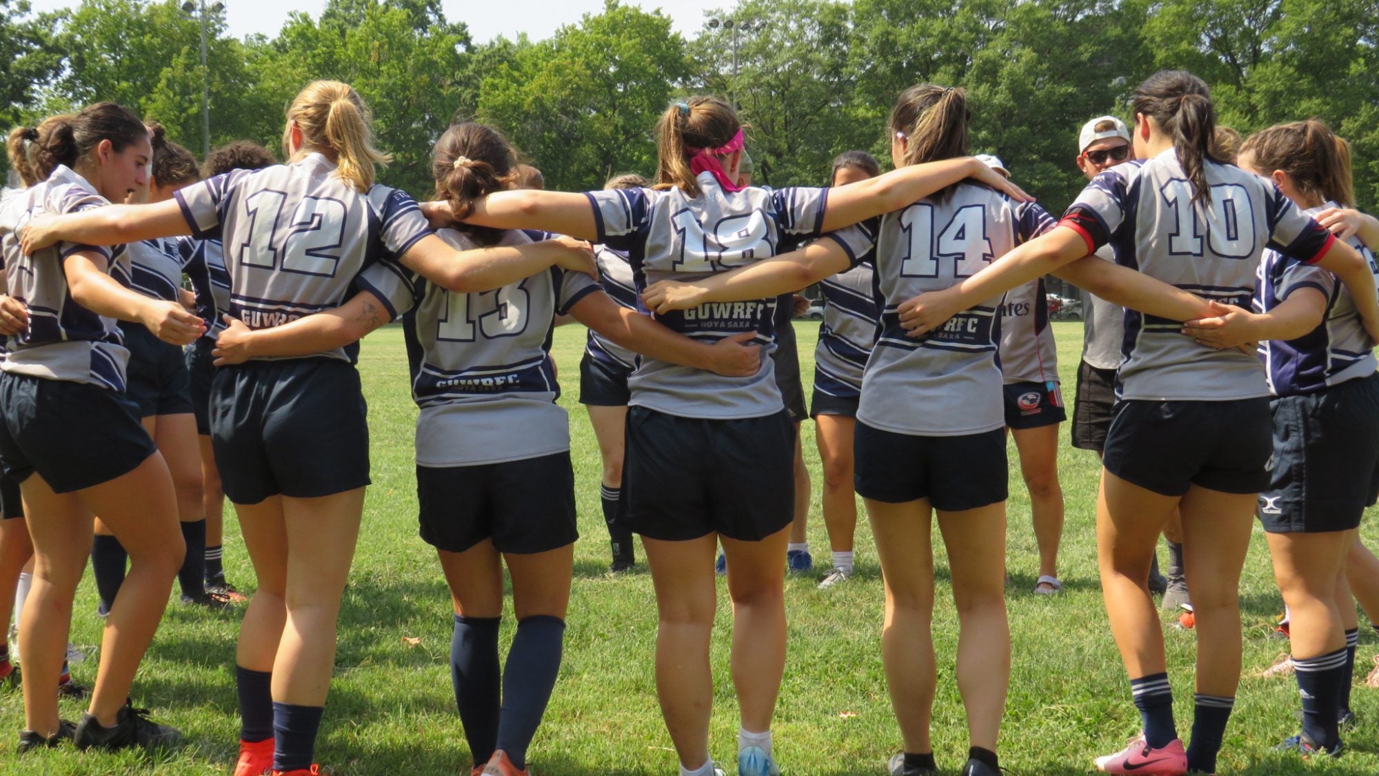 Team of women in a circle with locked arms ready to play rugby