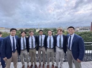 7 young men in matching blue suits and ties with the Washington Monument in the background