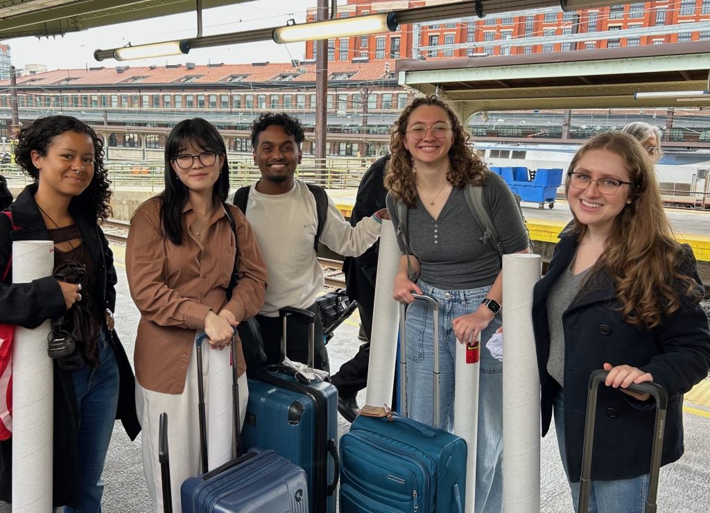 A group of students hold luggage at a train station