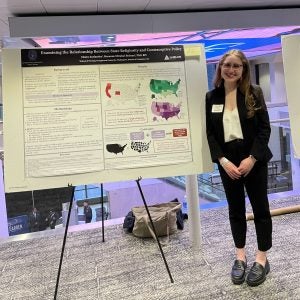 A student stands next to a poster of her research and smiles