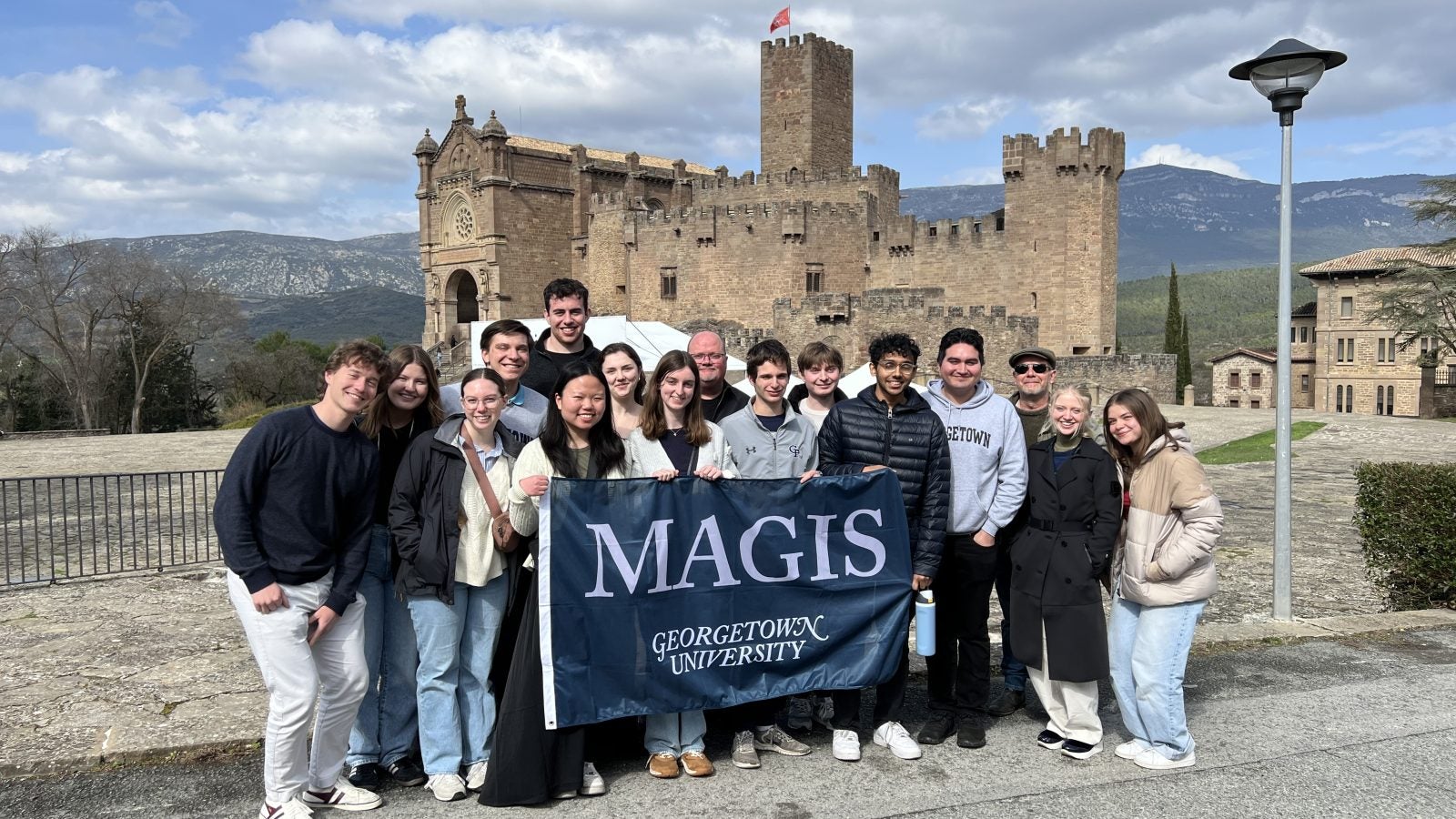 Students holding a Georgetown flag in front of a castle structure.