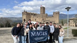 Students holding a Georgetown flag in front of a castle structure.