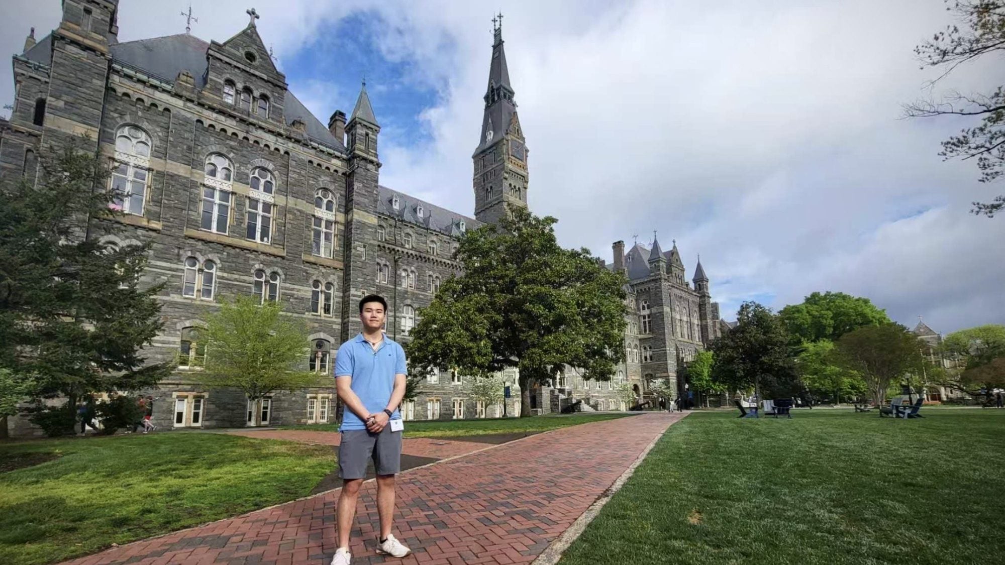 Young Asian man in blue shirt standing in front of Healy Hall on a sunny day