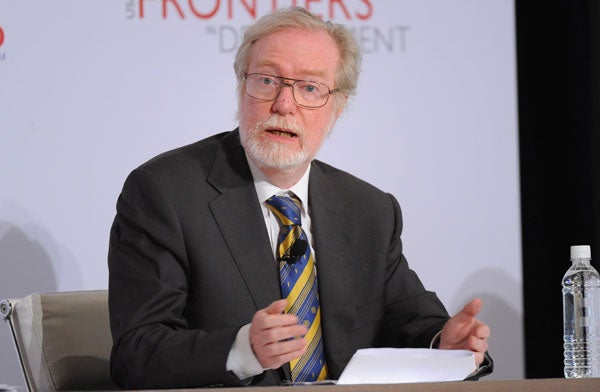 Paul Collier speaks into a microphone while standing in front of a backdrop