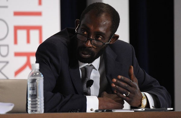 Njack Kane speaks while seated at a table with a microphone