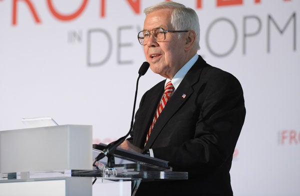 Richard Lugar speaks into a microphone in front of a backdrop