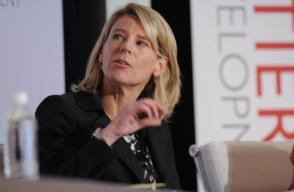 Carolyn Miles speaks and gestures while sitting in front of a backdrop