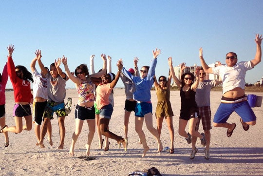 Students jump into the air for a photo while on the beach