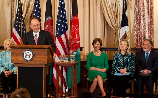 Melanne Verveer, Laura Bush, Hillary Clinton and Zalmai Rassoul sit behind U.S. and Afghan flags, John DeGioia speaks at podium 