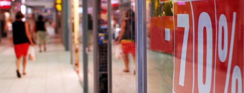 A photo of a women walking in a mall. A red 70% off sale sign is in focus in the foreground.